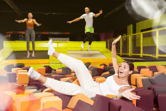 Happy excited young girl playfully diving into colorful foam cube pit at lively indoor trampoline park..