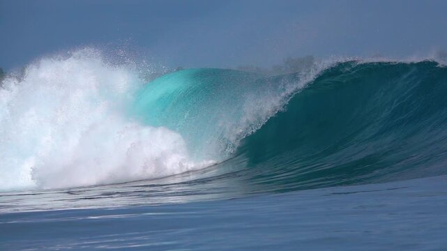 SLOW MOTION: Whitewater explodes beside a hollow blue barrelling wave as it races down the reef in the Mentawai Islands. Offshore mist and a smooth face emphasize the power and elegance of the ocean.