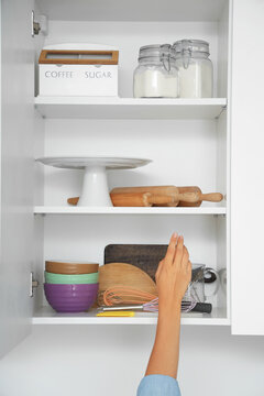 Woman opening kitchen cupboard with ingredients and set of kitchen utensils for bakery