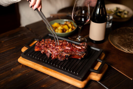 Sliced beef tagliata with tongs on cast iron grill pan with red wine and roasted potatoes in restaurant
