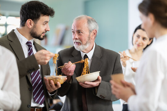 Positive two male office workers eating food together during lunch time in bright office of business company