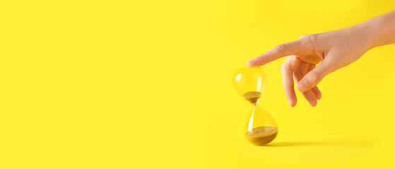Female hand with stylish hourglass on yellow background