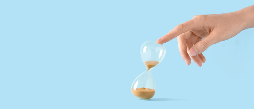 Female hand with yellow sand in stylish crystal hourglass on blue background