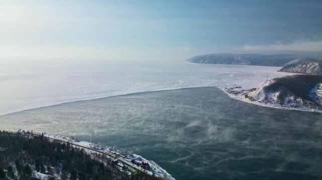 Aerial view of Listvyanka village and Angara River flowing into Lake Baikal in winter, Siberia. 
The Angara River flows into the frozen lake, creating a striking contrast between open water and ice. 