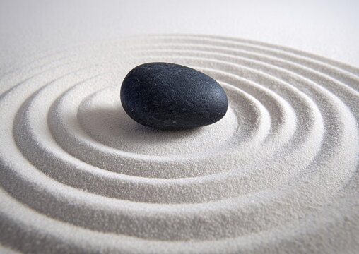 Smooth black stone in white sand with concentric circular raked patterns, zen garden close-up