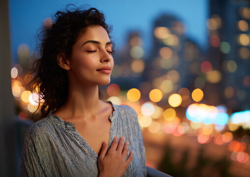 South Asian woman in 20s relaxing on a balcony at dusk with blurred city lights