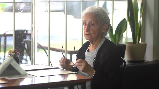 A grandmother sitting in a restaurant chair, putting on her glasses to read the menu
