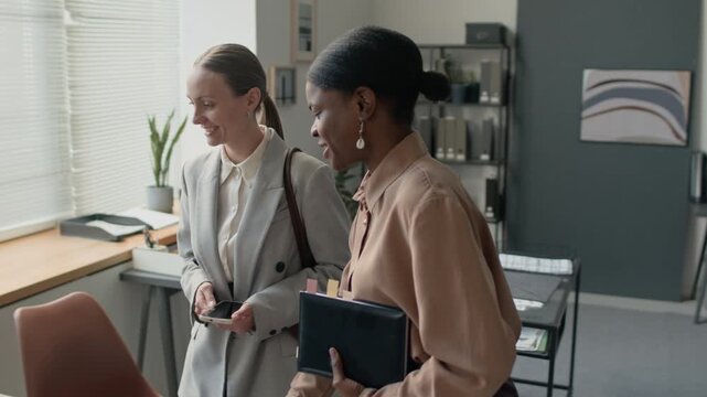 Young African American woman making tour to her newcomer colleague and showing her workstation in office