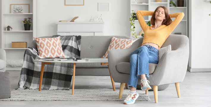 Young woman sitting in grey armchair at home
