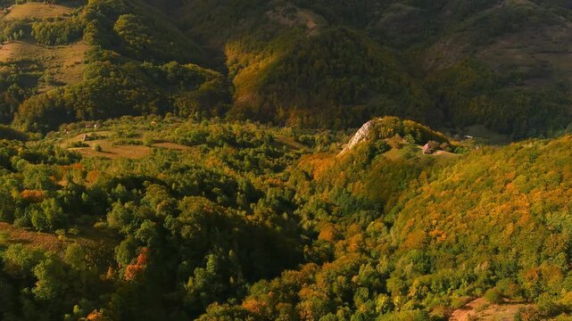 Aerial view of vibrant autumn forests covering the rolling hills and valleys with a small house on a ridge in Salciua de Jos, Alba County, Romania.