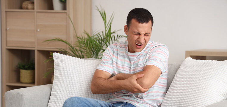 Young man suffering from pain in his elbow on sofa at home