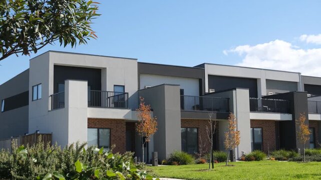A row of modern double-storey townhouses in a newly developed suburban estate in  Australia, overlooking a public green space or garden with&nbsp;lush green lawn.&nbsp;Medium density residential homes