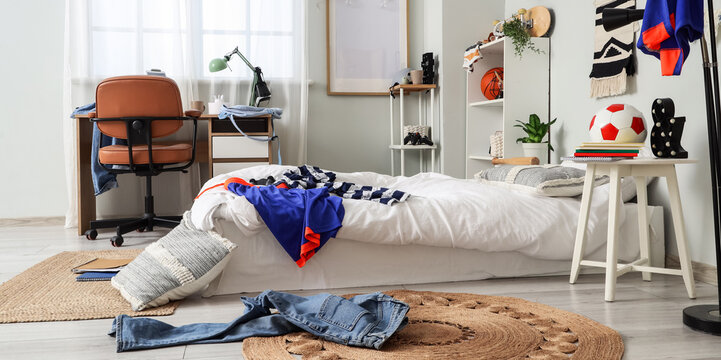 Interior of messy teenager's room with bed, workplace and shelf units