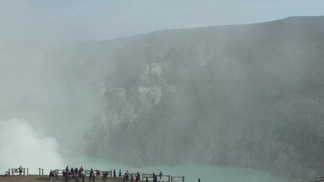 Aerial view of tourists walking along the crater rim fence with thick sulfur smoke rising from the volcano Kawah Ijen, East Java, Indonesia.