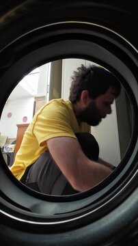 Unique point of view shot from inside of a young man loading clothes into the washing machine. Daily household chore or laundry routine