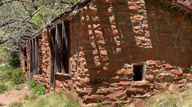 🏚️ Sedona Heritage: Abandoned Red Stone Cabin in Arizona. Surrounded by lush forest and majestic Sedona mountains under a blue sky. Sunny day, hiking trail, and ghost town vibe.