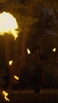 Solitary fire juggler performing at night in ornate costume, surrounded by swirling flames and glowing torches against a dark mysterious forest background