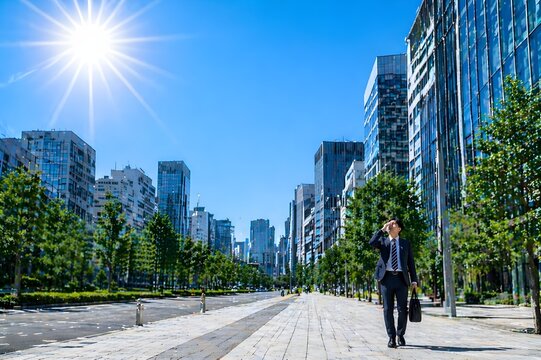 強い日差しのオフィス街を汗をぬぐいながら歩くスーツ姿の男性の猛暑と通勤ストレスイメージ（AI生成）