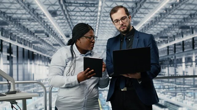 Businesspeople in microelectronics smart factory brainstorming to develop technology roadmaps. Teamworking employees using software on devices to upgrade semiconductor engineering tech, camera B