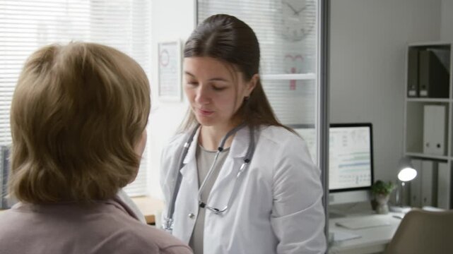 Tilt down shot of young female doctor wearing nitrile gloves checking pupil reaction with penlight while examining unrecognizable patient then filling out medical record on digital tablet at clinic