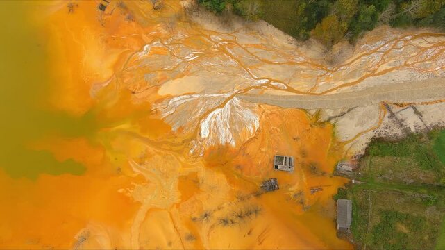 Aerial view of the toxic tailing pond with vibrant orange acidic water, sediment patterns, and submerged structures from the sunken village of Geamana. Geamana, Alba County, Romania.