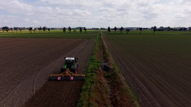Tractor ploughing field: A green tractor with a plough attachment is cultivating a vast brown field under a cloudy sky, preparing the soil for planting.