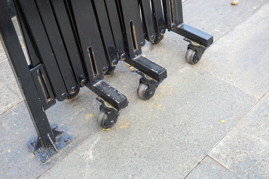 Detail of the wheel mechanism on the automatic folding gate made of black iron mounted on a gray natural stone floor, showing the mobility and security system of modern infrastructure.