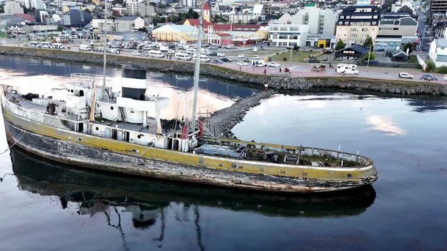 Cinematic drone orbit moving clockwise around the Saint Christopher shipwreck, revealing the industrial harbor, shipping containers, and Beagle Channel