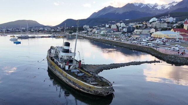Cinematic drone orbit of the historic Saint Christopher shipwreck, revealing the Ushuaia city skyline and snow-capped Martial Mountains in Argentina