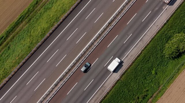 Highway aerial view: An aerial perspective captures the flow of traffic on a multi-lane highway, with cars and a truck navigating the asphalt under a clear sky, bordered by green fields and trees.