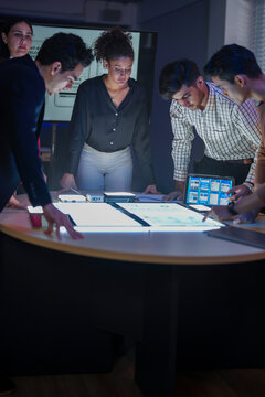 Diverse tech team brainstorming UI/UX mobile app wireframes. Creative developers collaborating on digital web design at glowing table in dark office.