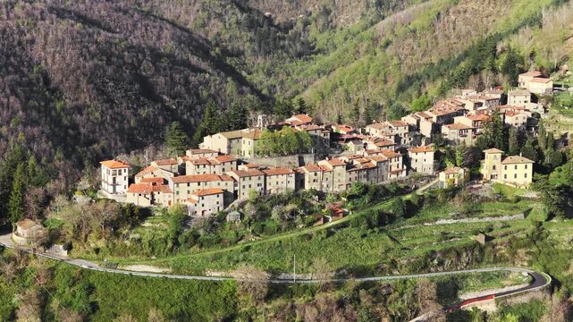 Aerial view of the historic stone village of Trappola nestled on a lush green hillside with terracotta roofs and dense forest Trappola, Tuscany, Italy.