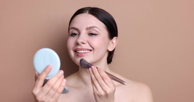 Woman applying foundation on her face with brush against beige background