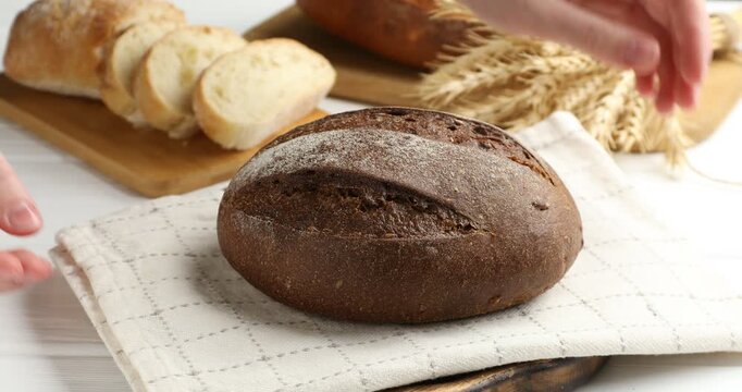 Woman putting loaf of rye bread on white wooden table, closeup