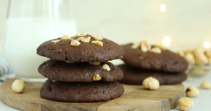 Woman taking tasty chocolate cookie with hazelnuts at table, closeup