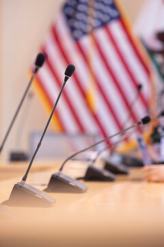 Microphones stand up in a board room with an American Flag background.