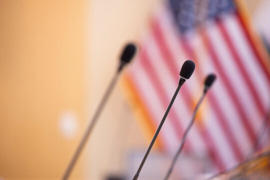 Microphones stand up in a board room with an American Flag background.