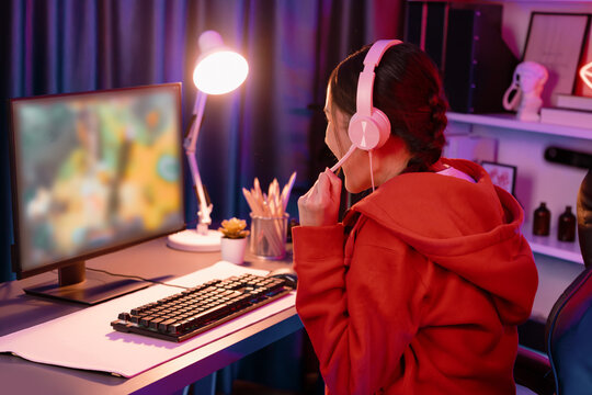 Host channel of young beautiful Asian gaming streamer playing fighting Moba at battle arena game on pc screen with multiplays, wearing pastel headphone at neon digital light modern room. Stratagem.
