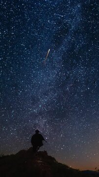 Man on a mountain top watching the night sky and celebrating shooting stars. Vertical design in 9:16 ratio. Smartphone and social media ready.
