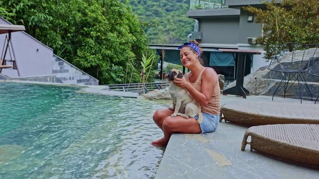 Smiling woman petting her pug dog by the pool