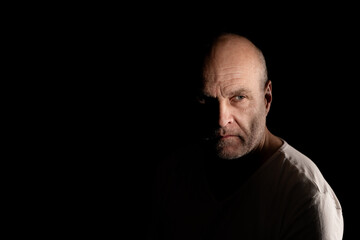 Obraz premium Serious bald man in low key lighting with mysterious shadows on his face