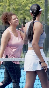 Vertical video: Walking woman crop skort holding paddle urging pink tank to greet at net on court