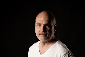 Obraz premium Mature bald man with stubble looking directly at camera against a dark background