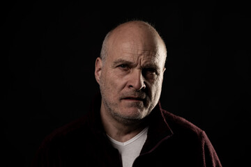 Obraz premium Older man expressing deep thought and seriousness on a black background, facing the viewer
