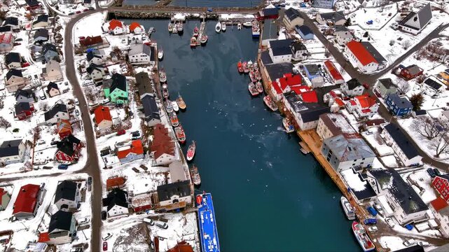 Aerial view of a traditional fishing village with colorful houses and boats docked in a narrow waterway surrounded by snow-covered terrain in Nordland, Norway.