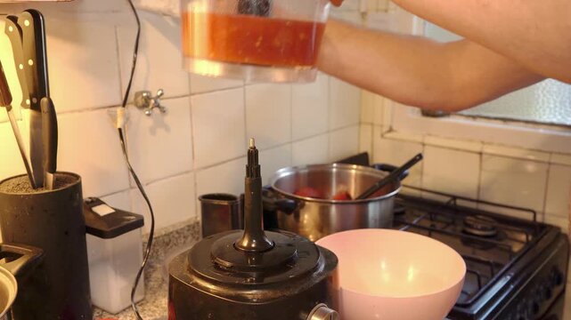 cook pouring crushed tomatoes from a food processor jug into a bowl