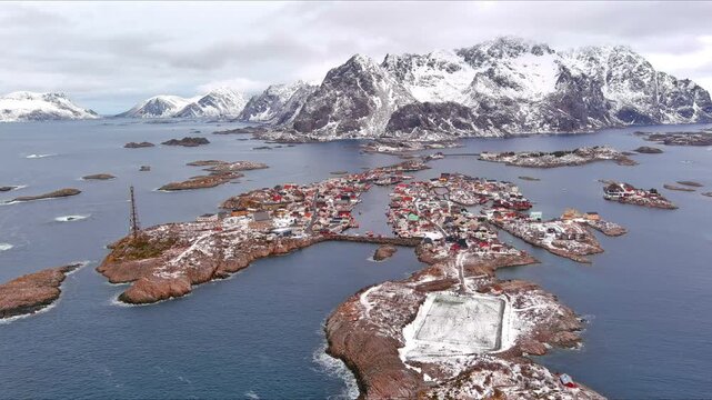 Aerial view of the fishing village of Henningsvaer with its famous football pitch on a rocky island surrounded by snowy mountains and the arctic sea in Nordland, Norway.