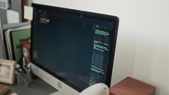 High angle no people close up shot of monitor displaying code, surrounded by stack of folders, and office supplies