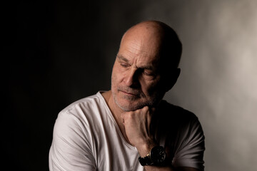 Obraz premium Mature man with closed eyes contemplating, chin resting on hand, dark background