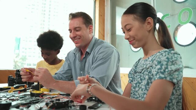 Skilled teacher explain about electric equipment to african boy while high school girl fixing model. Multicultural student learning about robotic car construction and electronic tool. Edification